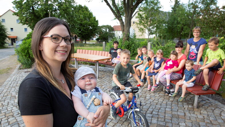 Elf von 21 Kindern kamen zum Fototermin in die Dorfmitte des kleinsten Kamenzer Ortsteils: Mama Sabrina Bartz hat den jüngsten Hennersdorfer Nachwuchs auf dem Arm. Benjamin Pohst saust auf dem Fahrrad dazwischen.