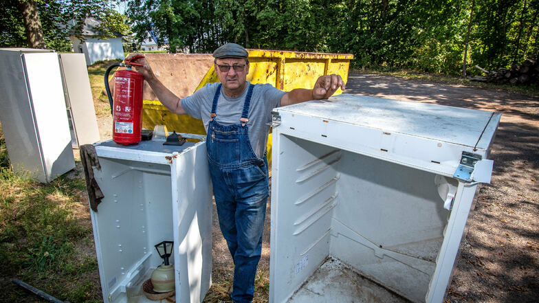 Firmenchef Klaus Dähne zeigt vier Kühlschränke und einen Feuerlöscher, die in oder neben seinem Container abgelegt worden sind.