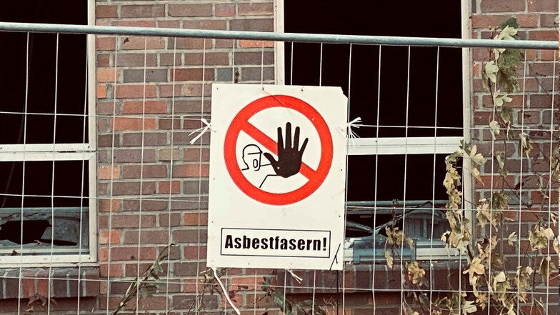 Ein Schild an einem Bauzaun warnt vor Asbestfasern.