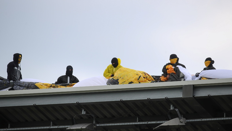 Auf dem Stadiondach bereiten Maskierte eine Choreografie vor - und sorgen damit für eine Verzögerung des Anpfiffs.