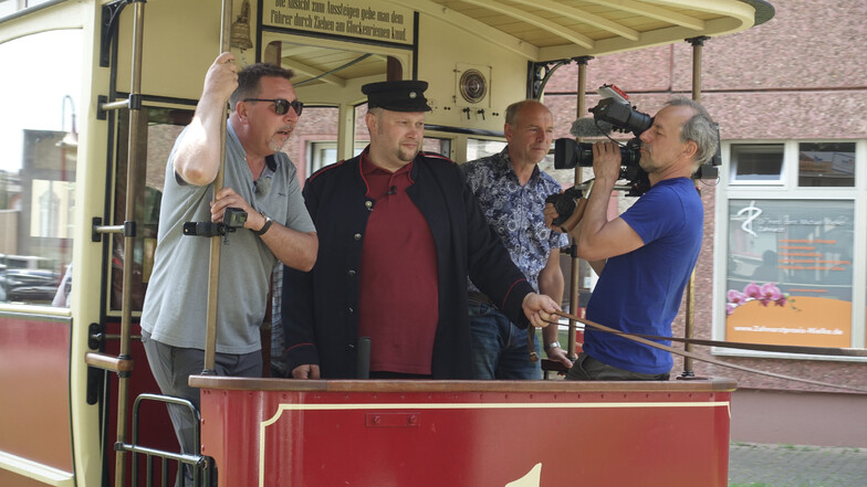 Thomas Böttcher (von links) steht mit Kutscher Mario Lommatzsch und dem Chef der Pferdebahner Jörg Lippert bei der Probefahrt auf dem Podest des historischen Pferdebahnwagens und wird gefilmt.