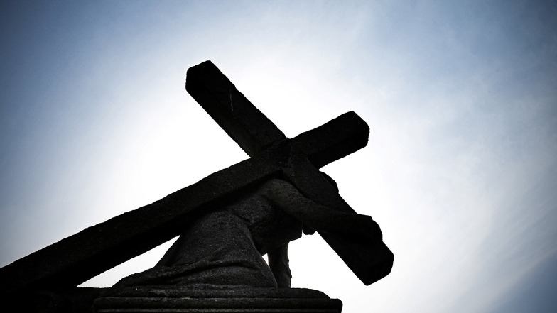 Eine Jesusstatue unter dem Kreuz zeichnet sich gegen die Sonne ab.