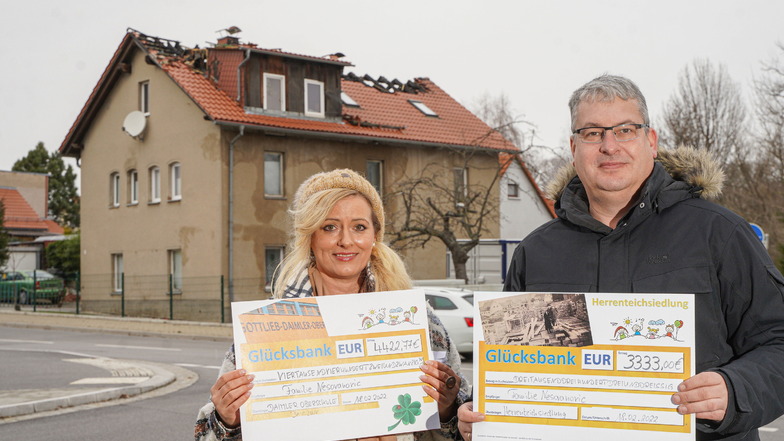 Annett Scholz-Michalowski und Jan Härta zeigen die Spendenschecks: Über 7.000 Euro wurden gesammelt, um der Familie zu helfen, deren Haus (im Hintergrund) an der Neustädter Straße in Bautzen nach einem Brand unbewohnbar ist.