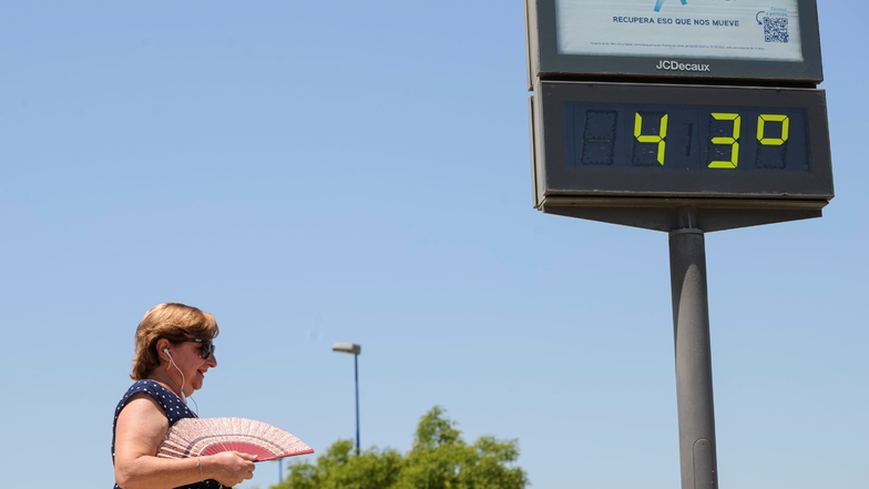 Eine Frau mit einem Handfächer läuft an einem öffentlichen Thermometer in Sevilla vorbei, das 43 Grad Celsius anzeigt. Die zweite Hitzewelle des Jahres hat begonnen.