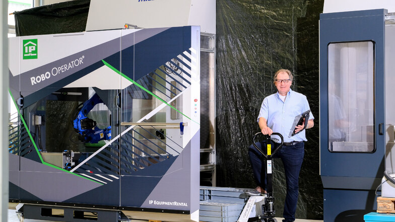 Ralf Hock, Geschäftsführer von Industrie-Partner Coswig, an einer Werkzeugmaschine, die von einem in der Firma entwickelten Roboter bedient wird.