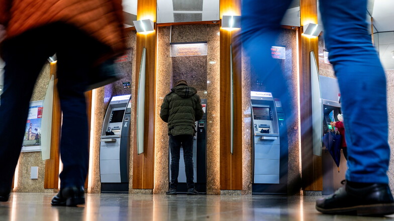Menschen gehen an Bankautomaten vorbei, während ein Mann Geld abhebt.