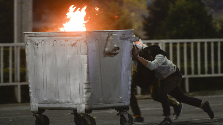Demonstranten schieben während einer Kundgebung eine brennende Mülltonne in Richtung der Polizei