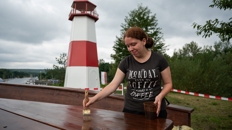 Lea Schmitz ist eine der Teilnehmerinnen in dem Projekt der Bao. Sie streicht das neue Holzboot an Land am Hafen in Tauchritz. Hinter ihr der neue Leuchtturm.