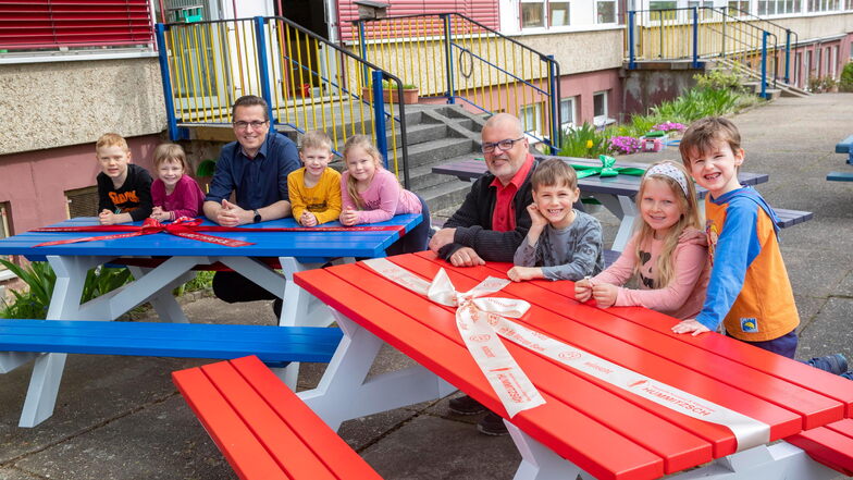 Ivo Kionka, Geschäftsführer der Firma Kurz Typofol, und Holger Hummitzsch, Geschäftsführer des Pflegedienstes Hummitzsch, sitzen mit Kindern des Kinderhauses Am Holländer an den neuen Sitzgarnituren im Garten.