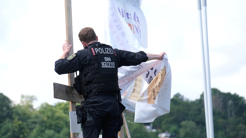 Ein Polizist entfernt das selbstgebastelte Plakat auf der Hafenstraße in Meißen, der Staatsschutz ermittelt aufgrund verfassungsfeindlicher Inhalte.