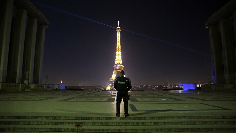 Frankreich, Paris: Ein Polizist patrouilliert am Trocadero vor dem beleuchteten Eiffelturm.