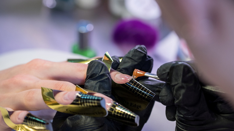 Eine Kosmetikerin trägt in einem Nagelstudio eine Gelschicht auf die Nägel einer Kundin auf.