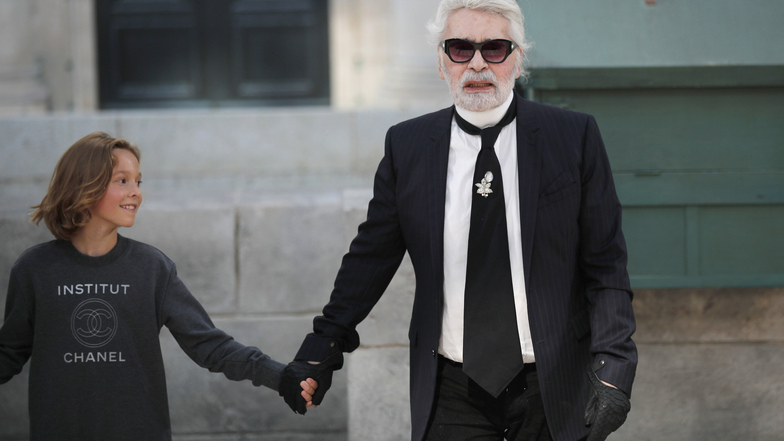 2018 mit seinem Patensohn, dem Model Hudson Kroenig, auf den Laufsteg nach der Präsentation seiner Kreationen des Modehauses Chanel im Rahmen der Haute-Couture-Schauen für Herbst/Winter 2018/2019 in Paris.  Foto: Francois Mori / AP / dpa
