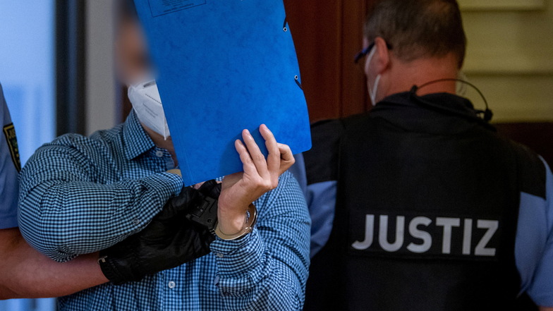 Ein angeklagter Mann wird von Justizpersonal in den Verhandlungssaal in Leipzig geführt. Die Staatsanwaltschaft wirft dem 34 Jahre alten Angeklagten vor, im November 2020 einem 52-Jährigen ein Messer in die Schläfe gerammt zu haben - vor den Augen des