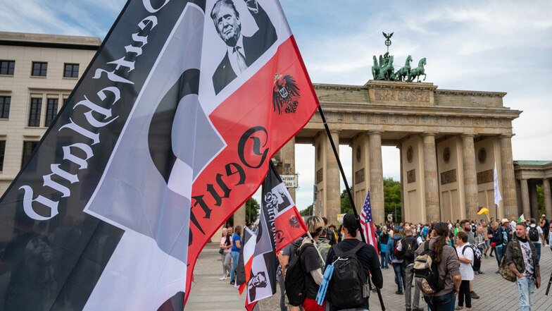 Ein Demonstrant hält vor einer Demonstration gegen die Corona-Maßnahmen eine große Reichsflagge mit dem Konterfei von US-Präsident Donald Trump vor dem Brandenburger Tor.