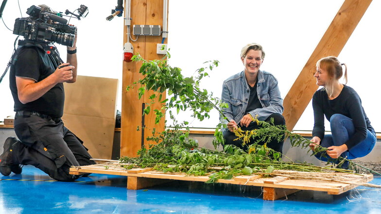 Moderatorin Laura Kampf und Henriette Uhlig (rechts) hocken vor einem Pflanzen-Haufen, aus dem Produkte hergestellt werden können.