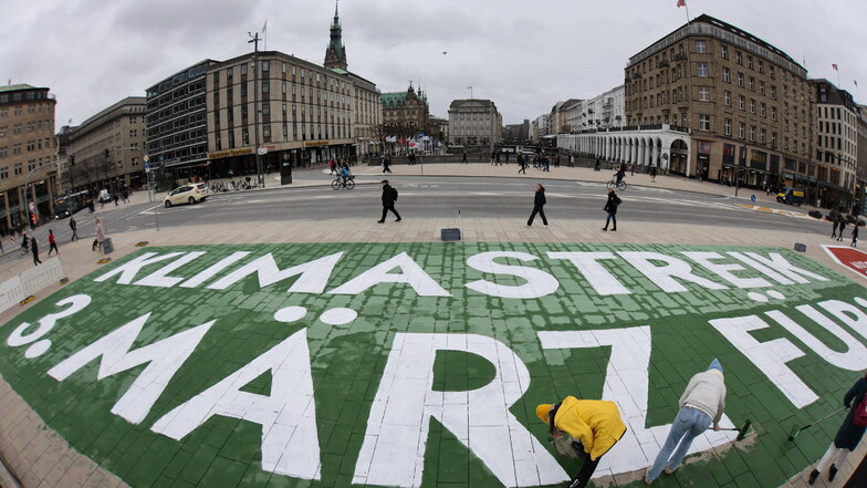 Mitstreiter der Klimabewegung Fridays for Future malen einen Protesttext auf den Jungfernstieg nahe des Hamburger Rathauses. Heute steht der globale Aktionstag an.