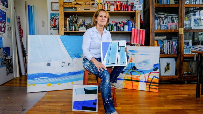 Sophie Cau mit aktuellen Arbeiten in ihrem Atelier in Radebeul. Hinter ihr stehen großformatig die Werke "grand large" und "free!", am Stuhl lehnt die Grafik "silence".