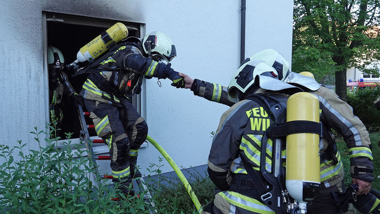 Ein Feuerwehrmann steigt aus dem Fenster der Brandwohnung in Kesselsdorf.