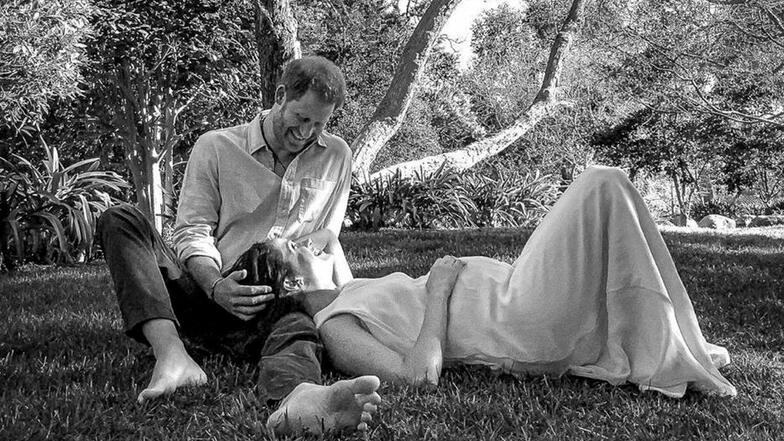 Prinz Harry und seine Frau Herzogin Meghan in einer romantischen Pose in einem Park.