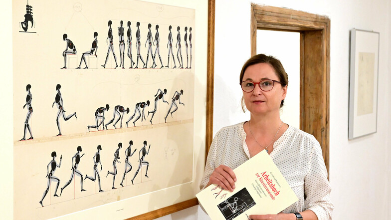 Anke Stenzel, jüngste Tochter von Gottfried Bammes, steht im Einnehmerhaus neben Bewegungsabläufen, die ihr Vater 1957 für das Buch „Die Gestalt des Menschen“ stempelte und malte.