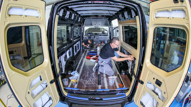 Zwei Mitarbeiter des MAN Bus Modification Centers (BMC) bauen eine Elektro-Kleinbus eTGE mit einer besonderen Innenverkleidung für den Personentransport aus. Rote bzw. blaue Ambientebeleuchtung erzeugen warme oder kühle Stimmung und helfen so, den Klimati