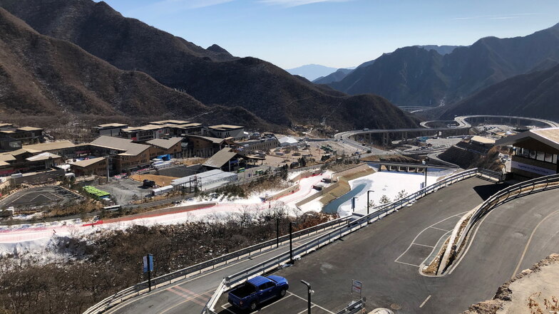 Zwischen Bergen im chinesischen Nirgendwo ist das neue Wintersportzentrum entstanden, fotografiert vom Start des Eiskanals. Links das Olympische Dorf, das später für den Tourismus genutzt werden soll. Die Abfahrtspiste führt bis zur Eingangstür.