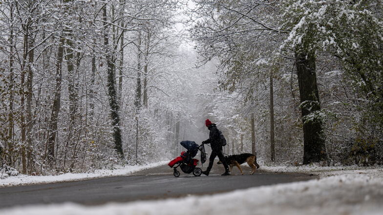 Eine Frau mit Kinderwagen überquert eine verschneite Straße in Leipzig. Der Winter gibt in Sachsen nur ein kurzes Intermezzo.