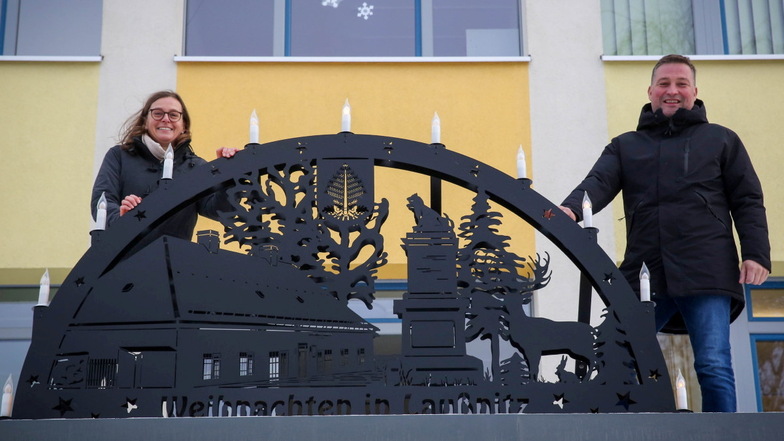 Gemeinderätin Kati Schlegel und Bürgermeister René Georgi sind aufs Vordach der Laußnitzer Grundschule gestiegen, um den besonderen Schwibbogen zu präsentieren.