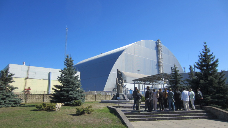 Eine Touristengruppe steht am Mahnmal vor dem 1986 explodierten Block vier des Atomkraftwerks Tschernobyl in der Ukraine.