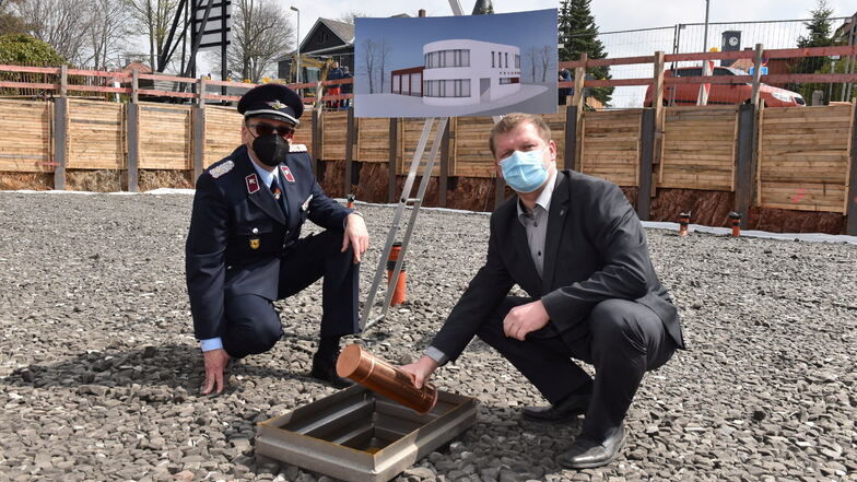 Bürgermeister Thomas Paul (rechts) und Gemeindewehrleiter Armin Groß versenken die Zeitkapsel im Fundament.