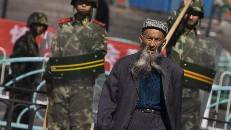 ARCHIV - 07.07.2009, China, Ürümqi: Ein Angehöriger der uigurischen Minderheit in China geht in der Unruheregion Xinjiang in Nordwestchina vorbei an chinesischen Sicherheitskräften.