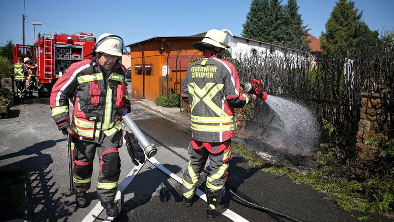 Feuerwehrleute löschen am Dienstag eine brennende Hecke in Struppen.