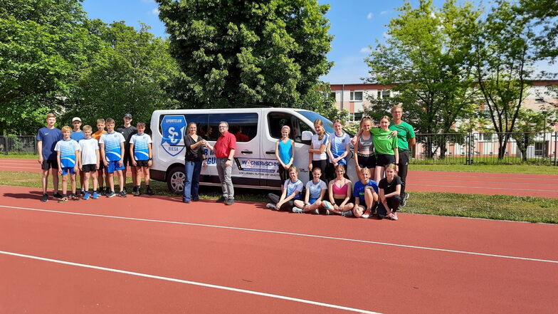 Die Trainingsgruppe Leichtathletik und Katja Hänchen von der SC-Riesa-Geschäftsstelle freuen sich über den neuen Bus, den Andreas Wagner vom Autohaus Wagner + Schmid übergibt.