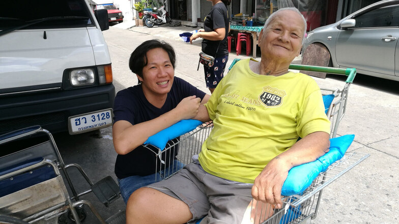Der thailändische Marketing-Experte Apichai Inthutsingh (l) hockt neben einem Kunden, der in einem Einkaufswagen sitzt, der zu einem Billig-Rollstuhl umgebaut wurde.