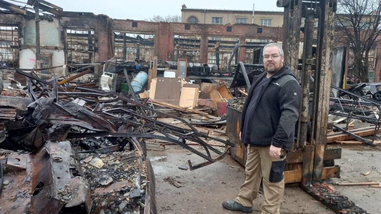 Werkstattwichtel Dirk Krause vor seinem verbrannten Gabelstapler und der Halle, in der sich seine Werkstatt befand.