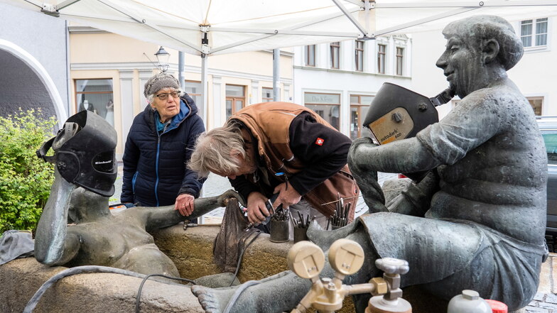 Die Görlitzer Künstlerin Gisela Mauermann, die den Brunnen kurz vor der Jahrtausendwende schuf, schaut Bert Noack von der Bronzegießerei Noack aus Leipzig zu, wie er das neue Handtuch am Brunnen auf dem Klosterplatz befestigt.