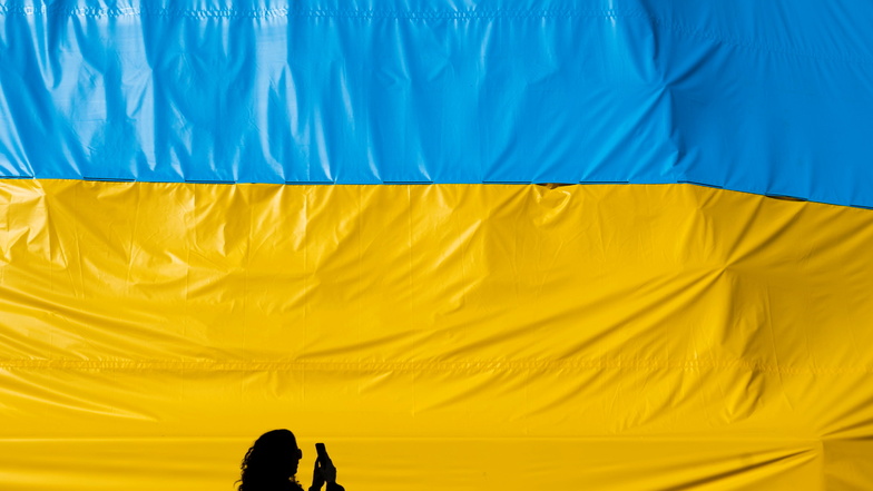 Eine Frau fotografiert in Prag ein Transparent in den Farben der ukrainischen Flagge.
