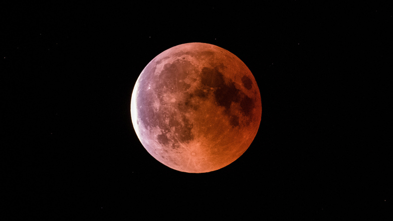 Der teilweise vom Erdschatten verdunkelte Vollmond leuchtet während einer Mondfinsternis rot bis orange.