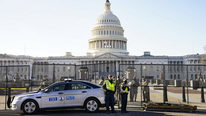 Soldaten und Polizeibeamte stehen vor dem US-Kapitol, während dort ein Sicherheitszaun errichtet wird.
