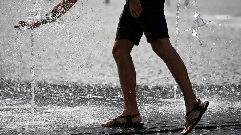 Bei heißen Temperaturen erfrischt sich ein Mann in Wasserfontänen.