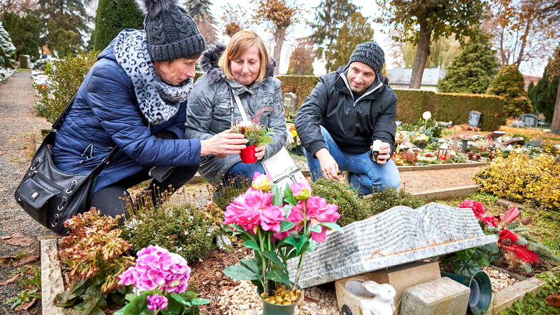 Auch Karin Letz (l.) aus Heidenau, Marion Reddel - deren Mann Dietmar 2019 an Krebs gestorben war und dort beerdigt wurde - und Robin Letz brachten eine Blume ans Grab auf dem Heidenauer Südfriedhof.