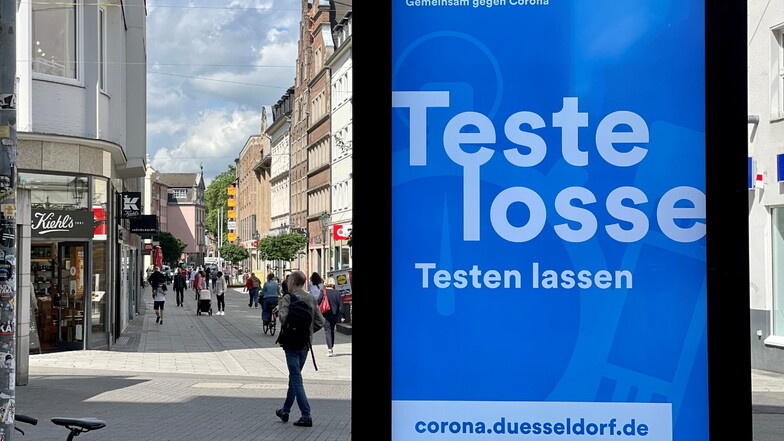 Ein digitales Werbeplakat fordert in rheinischer Mundart in der Düsseldorfer Altstadt zum Covid 19-Testen auf.