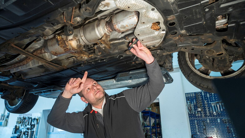 Klaus Pohlmann zeigt in seiner Zeithainer Werkstatt die Auspuffanlage eines Toyota. Hinter der silbernen Abdeckung versteckt sich der Katalysator.