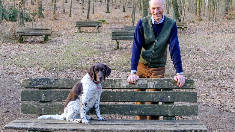 Stadtrat Hans Kraske (Freie Wähler) steht an einer Bank der Naturbühne bei Schwarzes Teich, auf der sein Hund Platz genommen hat. An den Sitzgelegenheiten nagt unübersehbar der Zahn der Zeit.