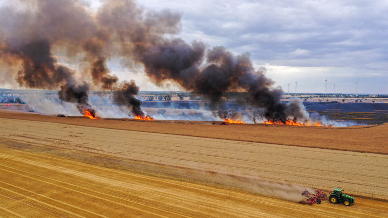 Mit einem Traktor pflügt ein Landwirt einen Schutzstreifen während eines Feldbrandes in ein Getreidefeld.