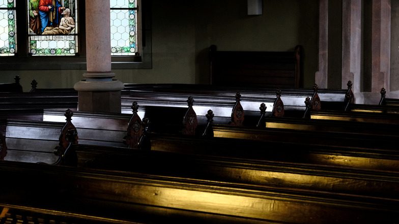 Das warme Licht fällt durch die Fenster auf das Gestühl im Kirchenschiff.