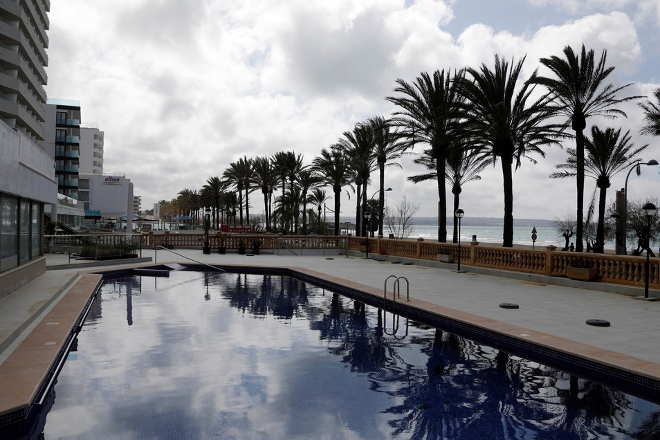 Palm trees are reflected in the pool of a closed hotel on Arenal Beach.